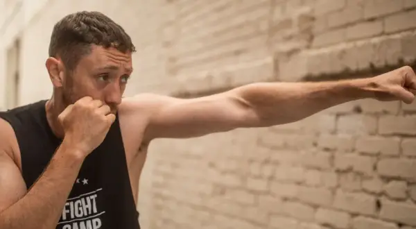 Man practicing boxing, demonstrating how to increase punching power at home with a focused stance against a brick wall.