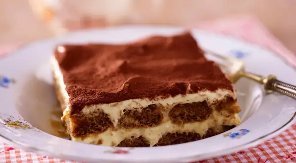 Ein Stück cremiges Tiramisu, das klassische italienische Dessert, bestäubt mit Kakao.