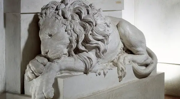 Leone scolpito, simbolo di forza, riposa ai piedi della tomba di Clemente XIII. La sua criniera fluente e le zampe possenti trasmettono un senso di maestà e quiete eterna.