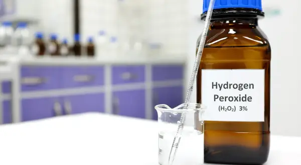 Butelka z H2O2 (nadtlenek wodoru) 3% i zlewka z płynem i pipetą w laboratorium.
