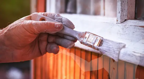 Main d'un peintre avec de la peinture blanche sur les doigts, tenant un pinceau. Astuces pour savoir comment enlever de la peinture sur les mains après le bricolage.