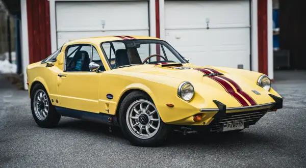 Gul Saab Sonett 2 med röda ränder, parkerad framför ett rött garage.
