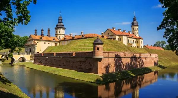 Zamek Mir, jedna z głównych atrakcji Białorusi, otoczony fosą i ceglanymi murami obronnymi, odbija się w spokojnej wodzie.