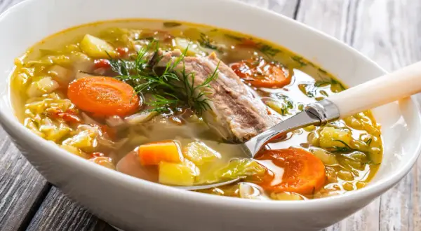 Aromaticzna zupa na żeberkach z warzywami i koperkiem, podana w białej misce na drewnianym stole.