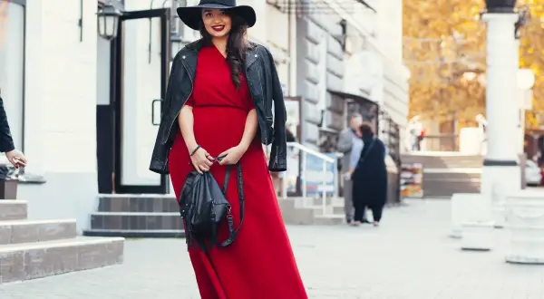 Kobieta w czerwonej sukni i czarnej ramonesce prezentuje stylowe stylizacje dla grubych nóg. Czarny kapelusz dodaje elegancji.