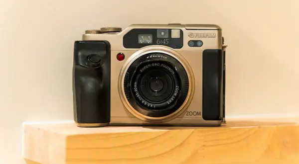 A gold Fujifilm 645 camera with a black grip sits on a wooden shelf.