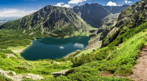 Bergsee in Polen, umgeben von grünen Hängen und schroffen Gipfeln. Die beste Reisezeit für solche Ausblicke ist der Sommer.