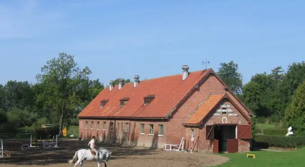 Jazda konna na tle ceglanej stajni z czerwonym dachem.