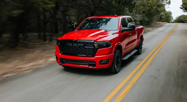 Czerwony Dodge Ram 1500 pędzi po krętej drodze wśród drzew.