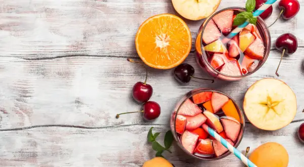 Sangria ricetta bar: bicchieri pieni di frutta fresca, arancia, mele, ciliegie e albicocche su un tavolo di legno.