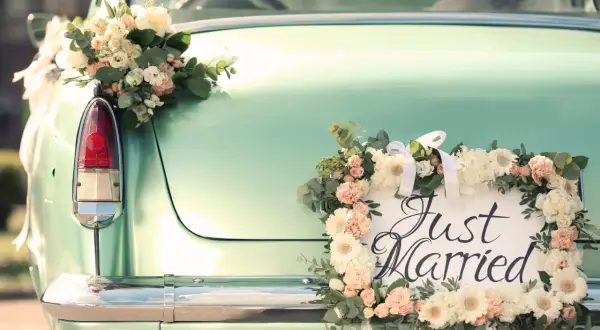 Hochzeitsauto mit Blumen geschmückt, "Just Married" Schild. Ein besonderer Urlaub nach der Hochzeit, vielleicht mit einem Kind auf dem Weg.