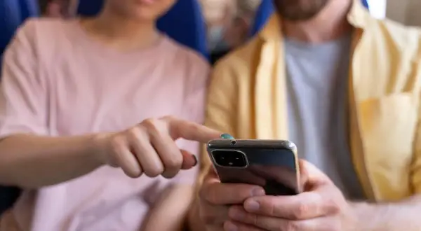 Pareja joven en un avión, compartiendo un teléfono. Quizás discutiendo sobre sus **relaciones parasociales** con influencers o celebridades.