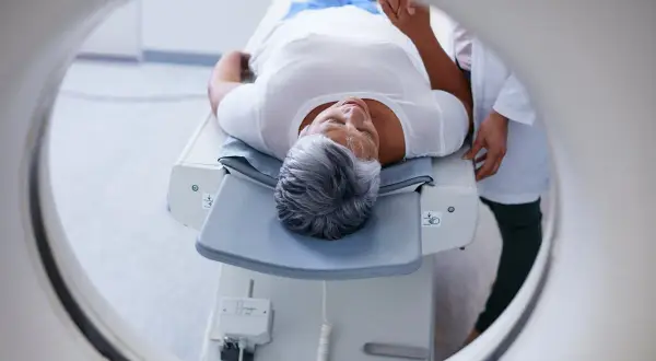 Une femme âgée se repose sur une table d'examen, prête pour un examen PET scan. C'est quoi un PET scan ? Une technique d'imagerie médicale.