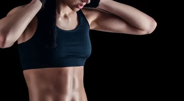 Donna con addominali scolpiti, che si sistema i capelli. Allenamento mirato per addominali senza sforzare la schiena.