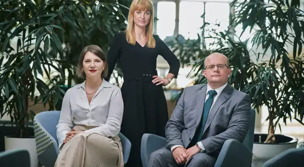 Trzy osoby w eleganckich strojach, otoczone zielenią. Zastanawiasz się, ile kosztuje prawnik? Oni mogą pomóc.