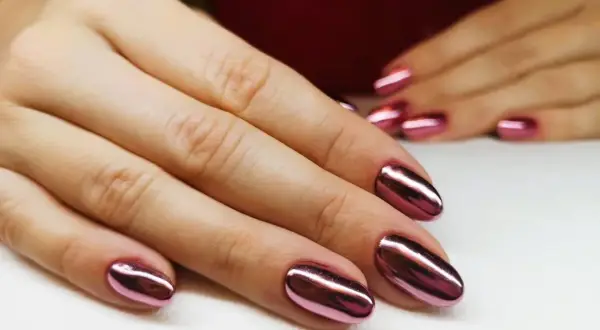 Dłonie z błyszczącym, metalicznym różowym manicure tytanowym. Czy ten efektowny manicure tytanowy rakotwórczy jest wart ryzyka?