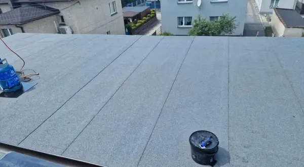 Nowy dach z papy na styropianie, gotowy na ochronę domu. Widać butlę gazową i wiadro z materiałami.