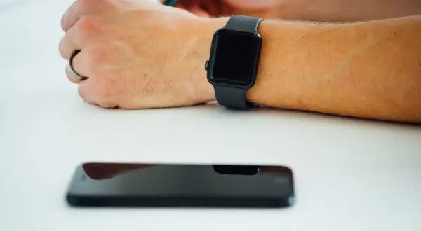 Czarny smartwatch na nadgarstku, obok leży wyłączony smartfon. Co zrobić, gdy smartwatch nie chce się włączyć?
