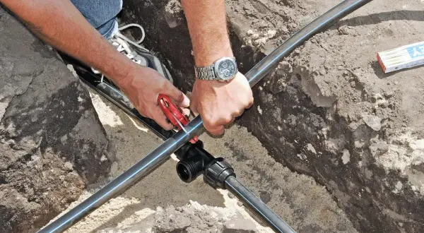 Hände schneiden Kunststoffrohr für die wasserleitung verlegen. Ein T-Stück wird vorbereitet.