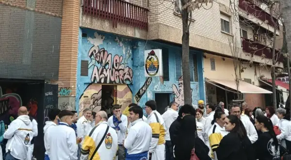 Gente reunida en la calle, algunos con chaquetas blancas y amarillas, celebrando la cincomarzada frente a un edificio con grafitis.