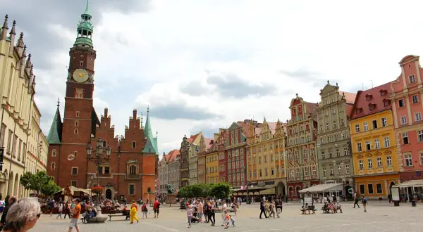Buntes Treiben auf dem Marktplatz der Breslau Innenstadt. Das Rathaus mit seinem markanten Turm dominiert die Szene, umgeben von farbenfrohen Bürgerhäusern.