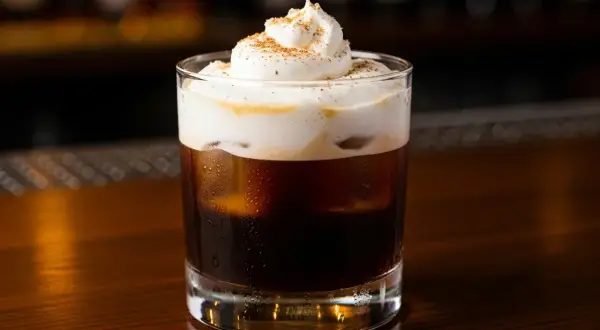 Ett glas med mörkt, isigt spanskt kaffe toppat med fluffig grädde och kanel.