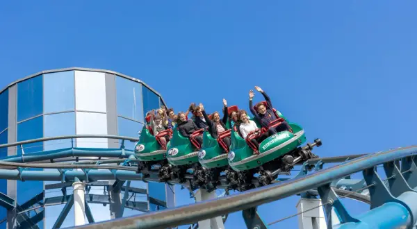 Ludzie na kolejce górskiej wesoło machają rękami. Dzięki **fastpass** uniknęli długiego czekania na tę ekscytującą przejażdżkę.