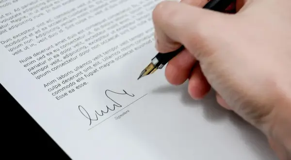 Dłoń podpisuje dokument, być może wypowiedzenie zmieniające warunki umowy.