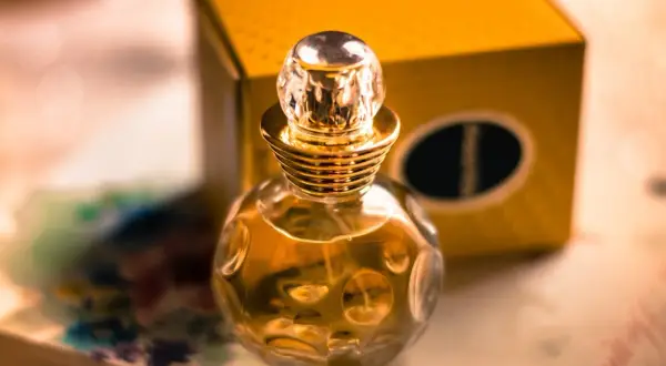 Złota buteleczka perfum Christian Dior Dolce Vita z kryształowym korkiem, obok żółtego pudełka.