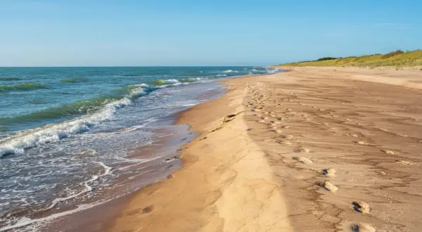Piękne, dzikie plaże nad Bałtykiem. Fale delikatnie obmywają piaszczysty brzeg, a na piasku widać ślady stóp.