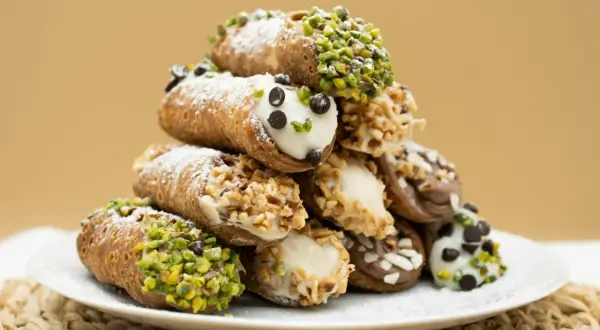 Stos idealnie udekorowanych cannoli z ricottą, posypanych cukrem pudrem, pistacjami i orzechami.