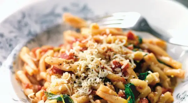 En skål med strozzapreti pasta, toppad med riven ost och en gaffel redo att hugga in.