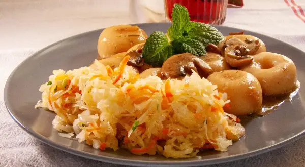 Pyszna surówka z kiszonej kapusty z marchewką, podana z duszonymi pieczarkami i kluskami śląskimi.
