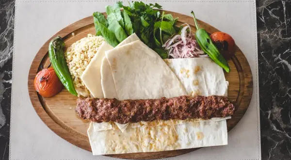 Pyszny kebab na szpadzie z ryżem, pieczonymi warzywami, świeżymi ziołami i cienkim pieczywem.