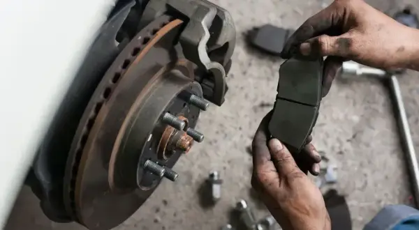 Mechanik trzyma zużyte klocki hamulcowe. Sprawdź wymiana klocków hamulcowych cena i zadbaj o bezpieczeństwo.