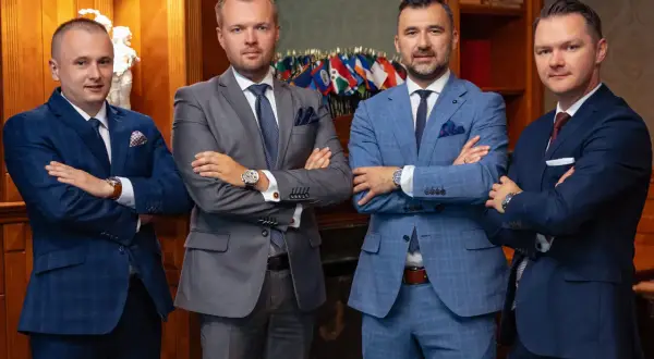 Czterech mężczyzn w garniturach stoi z założonymi rękami.