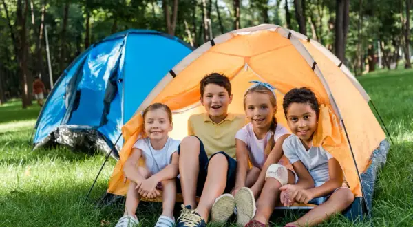 Niños sonríen en una tienda de campaña naranja, disfrutando de una acampada libre en Cantabria.