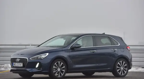 Ciemnoniebieski Hyundai i30 na parkingu. Kierowca w okularach siedzi za kierownicą, gotowy do wymiany żarówki.
