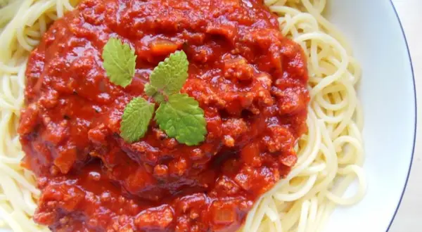 Spaghetti z bogatym sosem pomidorowym i mięsem mielonym, udekorowane listkami mięty.