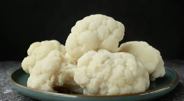 Coliflor cocida en un plato azul verdoso. El tiempo de cocción de la coliflor es clave para su textura.