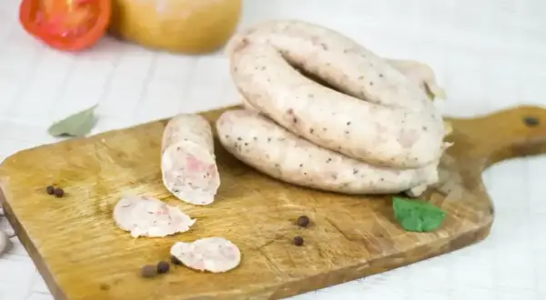 Swojska kiełbasa na desce, idealna na przepis 5 kg. Widoczne plastry, pieprz i liść laurowy.