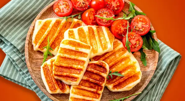 Grillowany ser halloumi z pomidorkami koktajlowymi na drewnianej desce.