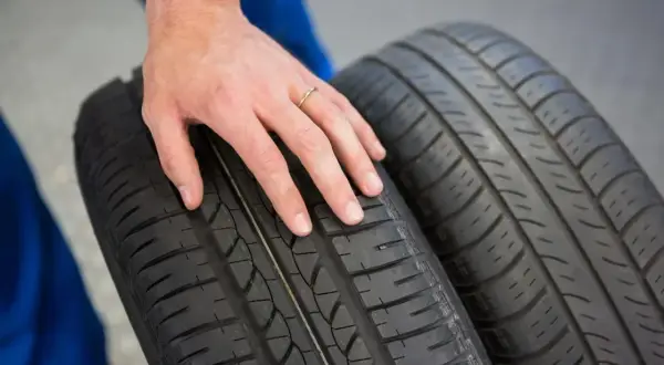 Dłoń mechanika dotyka bieżnika opony Hankook, sugerując pozytywne opony Hankook opinie.