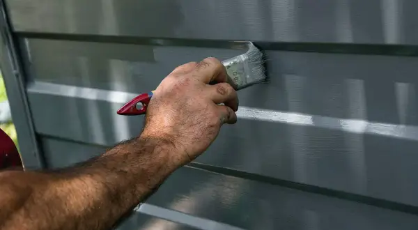 Mano che applica vernice grigia su una superficie a coste, probabilmente per verniciare alluminio e proteggerlo.