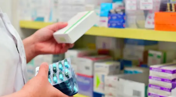 Farmaceuta trzyma opakowanie leku i kilka blistrów kapsułek. Pokazuje, ile ważna jest recepta i prawidłowe dawkowanie.