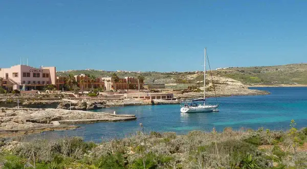Traumhafter Urlaub auf Malta: Ein Segelboot ankert in einer Bucht vor dem Comino Hotel, umgeben von Felsen und mediterraner Vegetation.