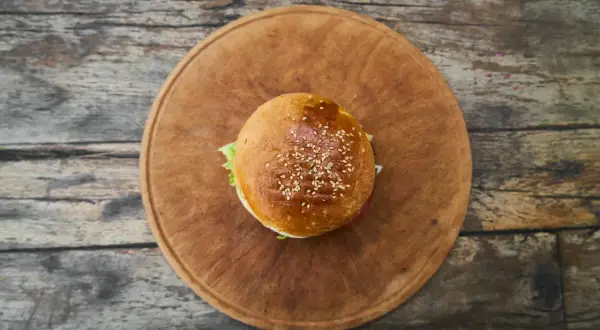 Hamburger z sezamem na drewnianej desce, widok z góry.