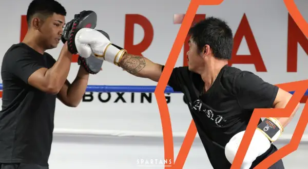 Two boxers train in a ring, one holding pads for the other's punch. This image shows the dedication required to reach advanced boxing levels.