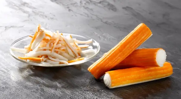 Surimi co to? Pomarańczowe paluszki i pokrojone w słupki surimi na talerzyku.