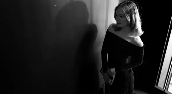 Eine Frau in einem eleganten, schulterfreien Kleid wartet im Schatten. Perfekt für einen Anlass mit "black tie optional"-Dresscode.